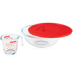 Clear Pyrex bowl with red lid and measuring cup on a white background
