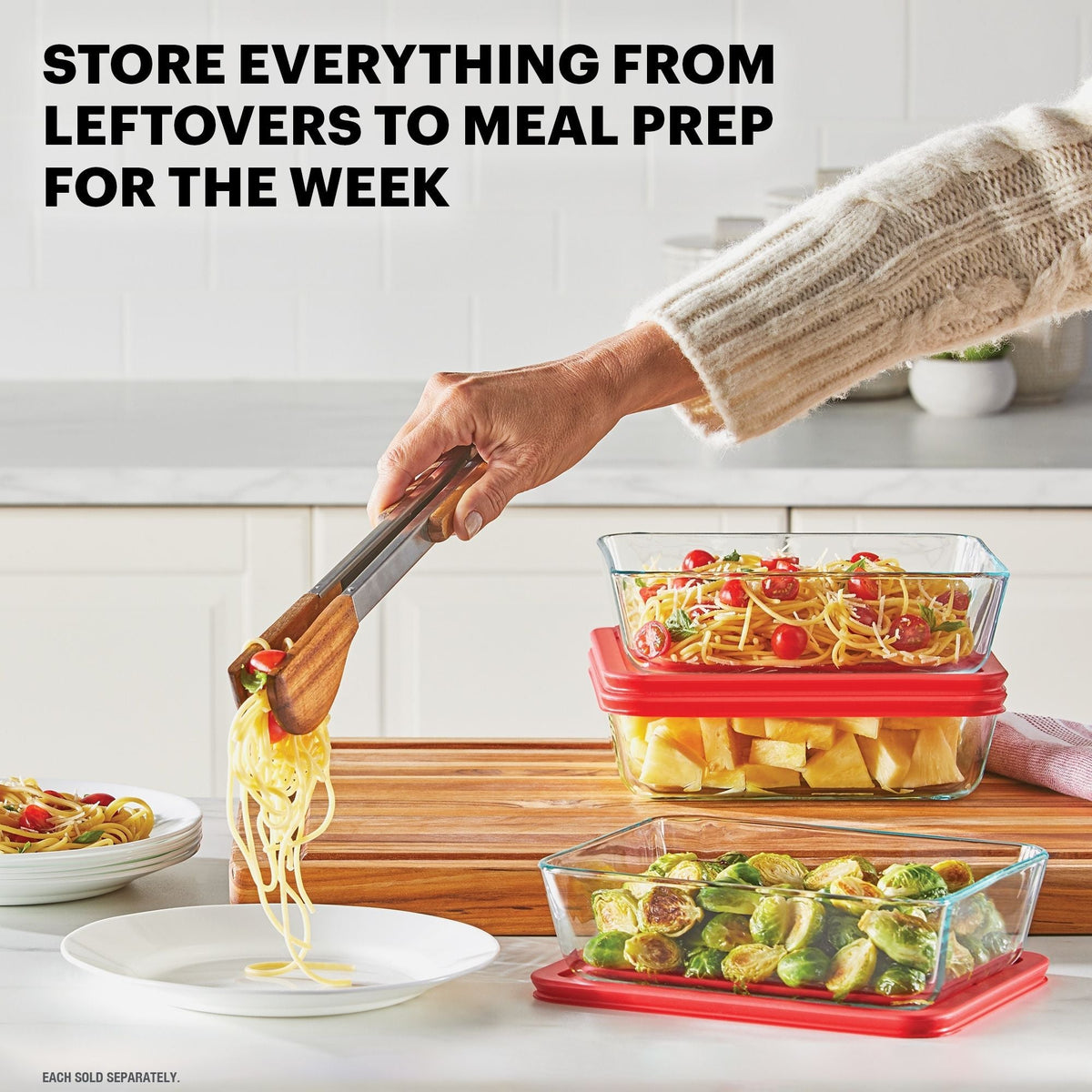 Person using tongs to serve pasta from a glass container with red lid, surrounded by other food containers on a kitchen counter.