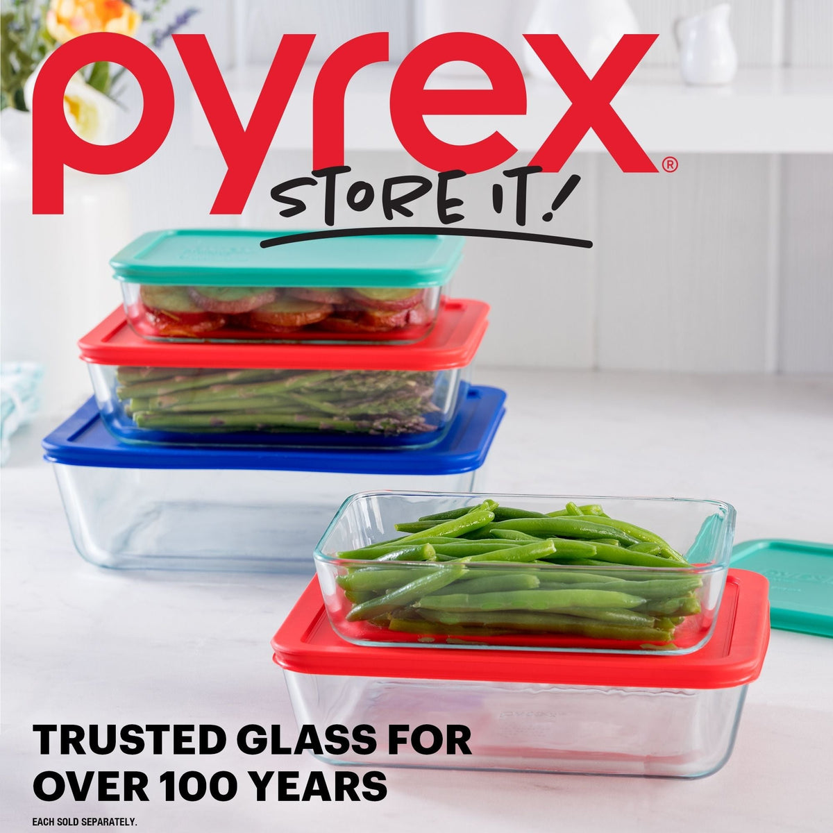 Pyrex food storage containers with colorful lids on a kitchen counter, featuring the Pyrex logo and branding.