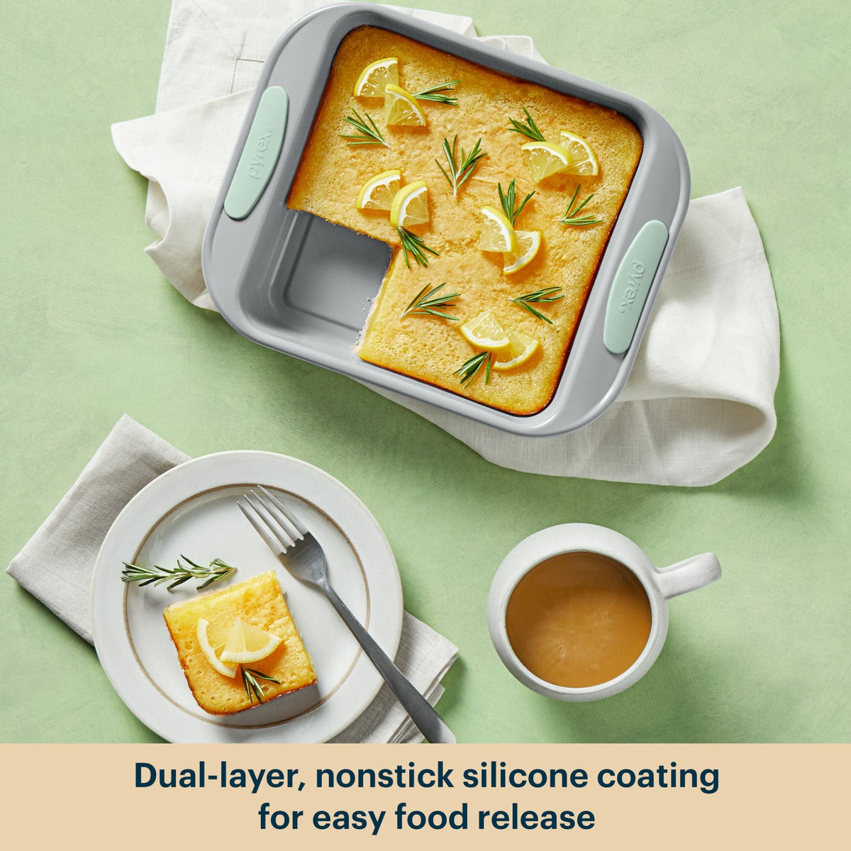 Baked dish in a gray silicone baking pan with lemon slices and rosemary on a green background.