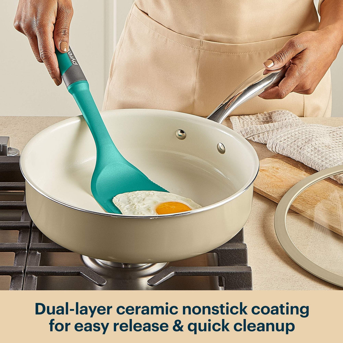 Person using a green spatula to stir eggs in a beige ceramic nonstick frying pan on a stove.