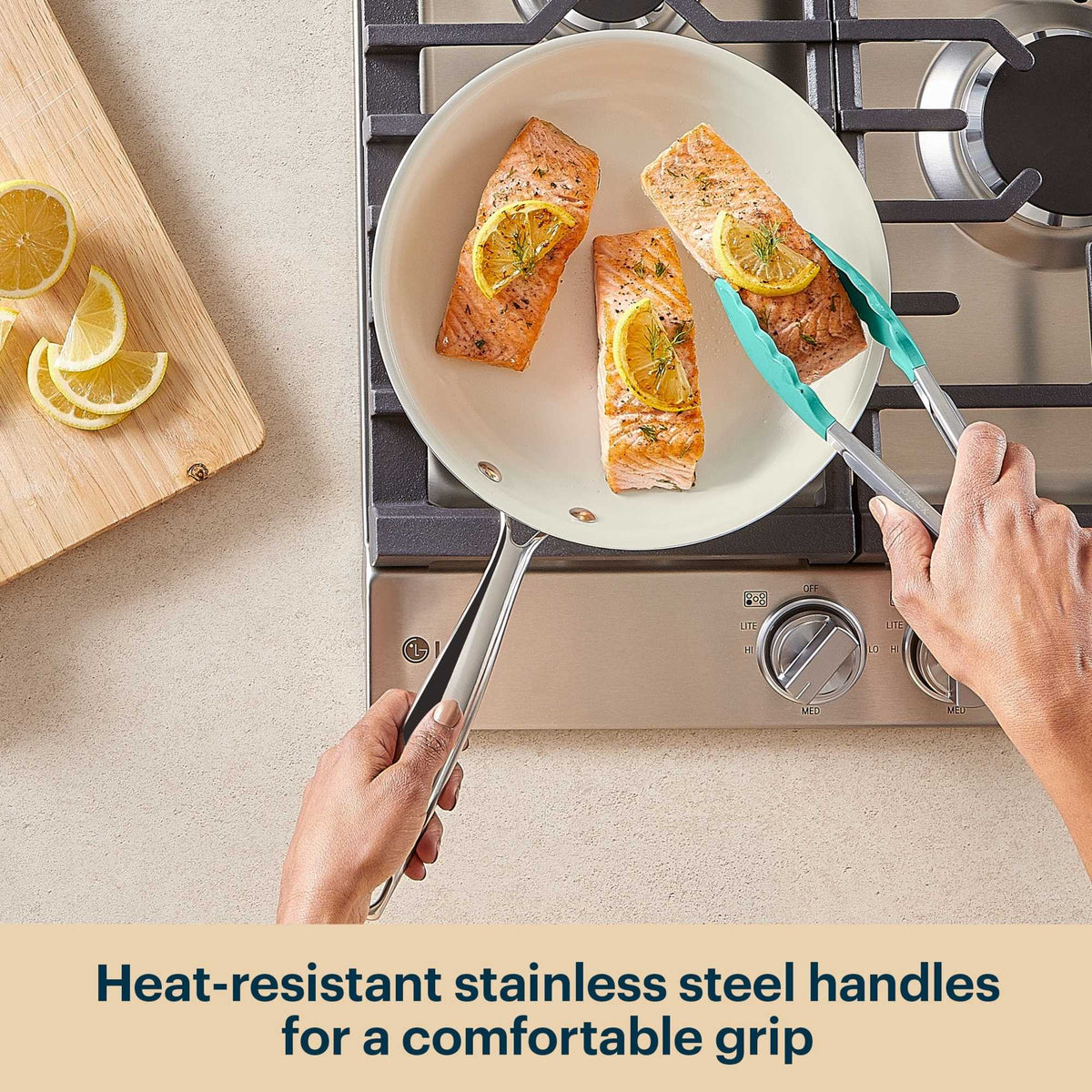 Person cooking salmon with lemon wedges on a stove using a pan with heat-resistant handles.