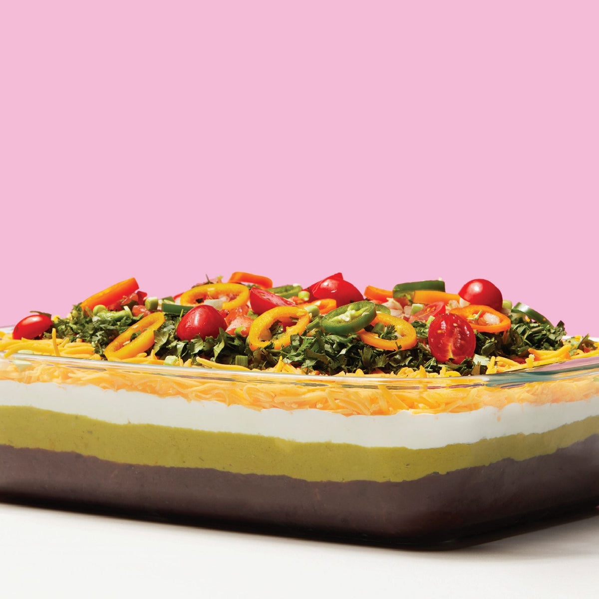 Layered salad in a glass dish with a pink background