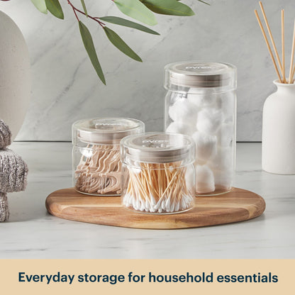 Clear jars with household essentials on a wooden tray with a neutral background