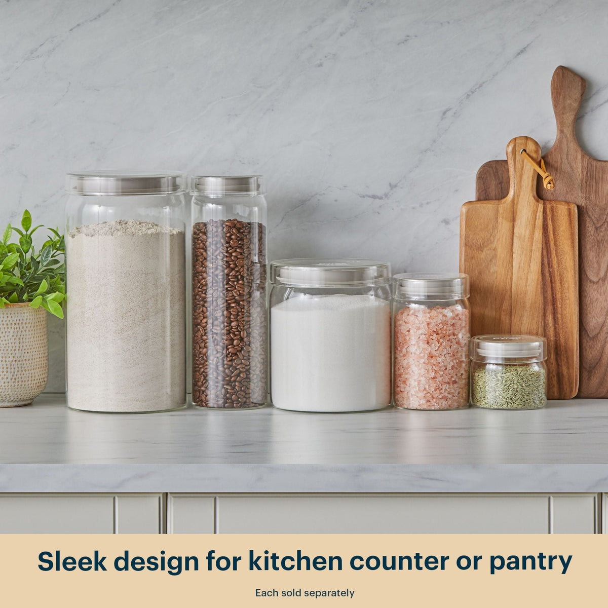 Glass jars with different contents on a kitchen counter with wooden cutting boards.